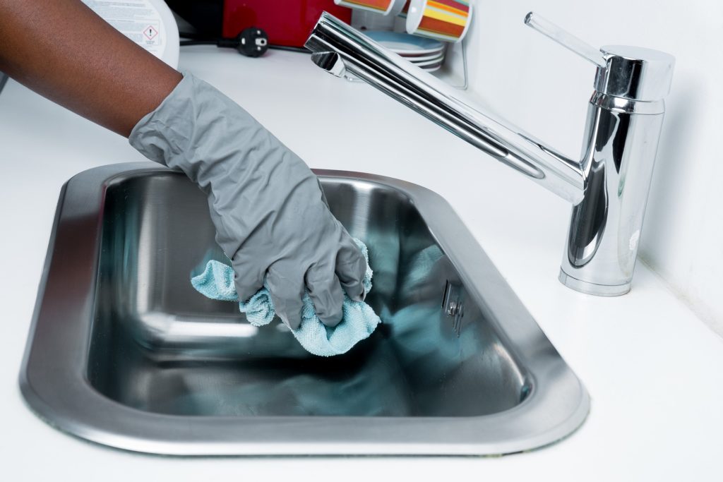 hand with rubber glove cleaning sink