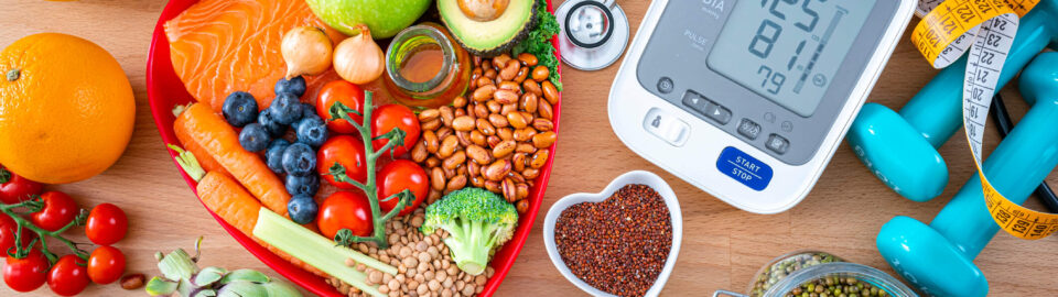 Tabletop filled with many different types of healthy foods & a digital blood pressure cuff